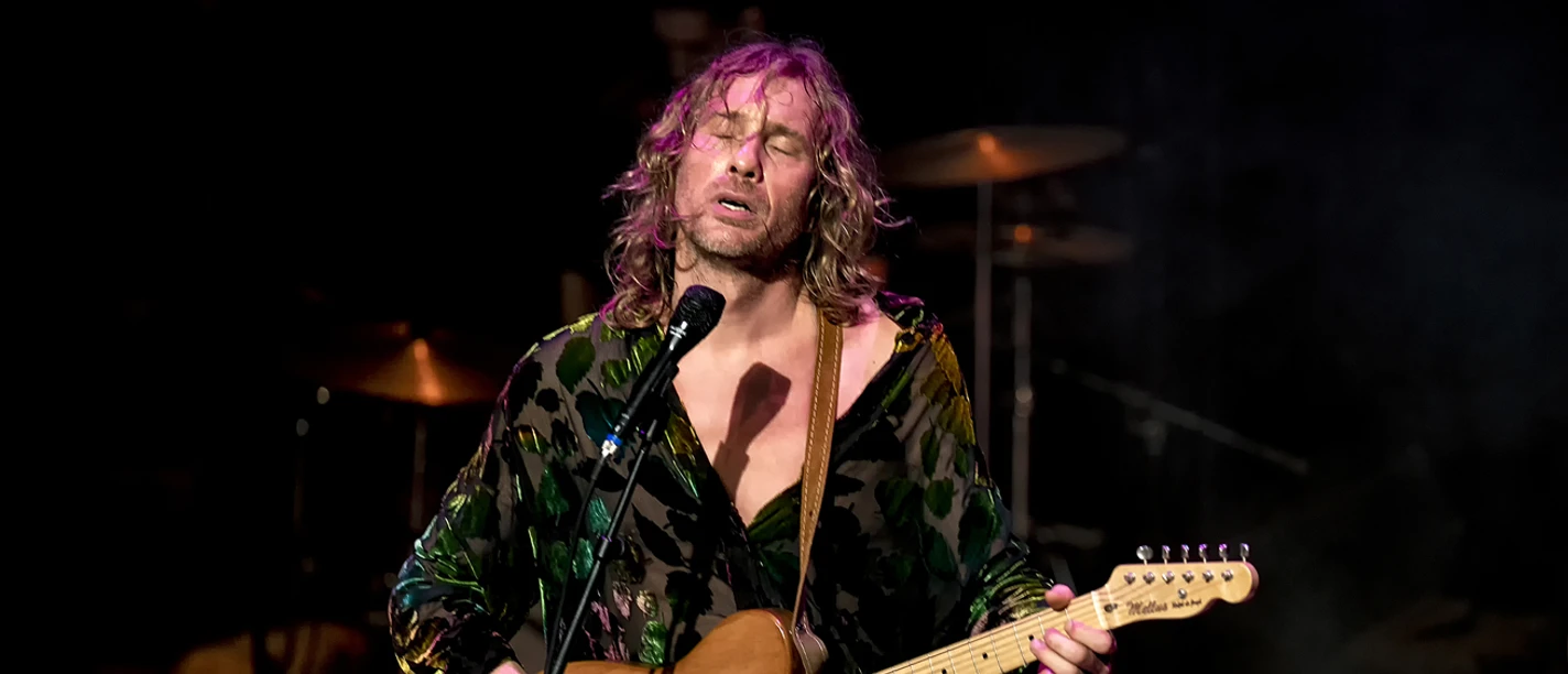 Ralph de Jongh singt auf der Bühne und spielt E-Gitarre im Scheinwerferlicht.