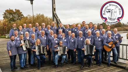 Fehntjer Shanty-Chor mit Akkordeons und Gitarre auf einer Holzterrasse am Wasser.