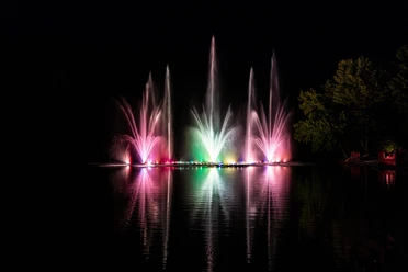 2025_Seefest-Behringen (4).jpg Bunte Wasserfontänen leuchten nachts über dem Brunausee in Behringen und spiegeln sich im Wasser.