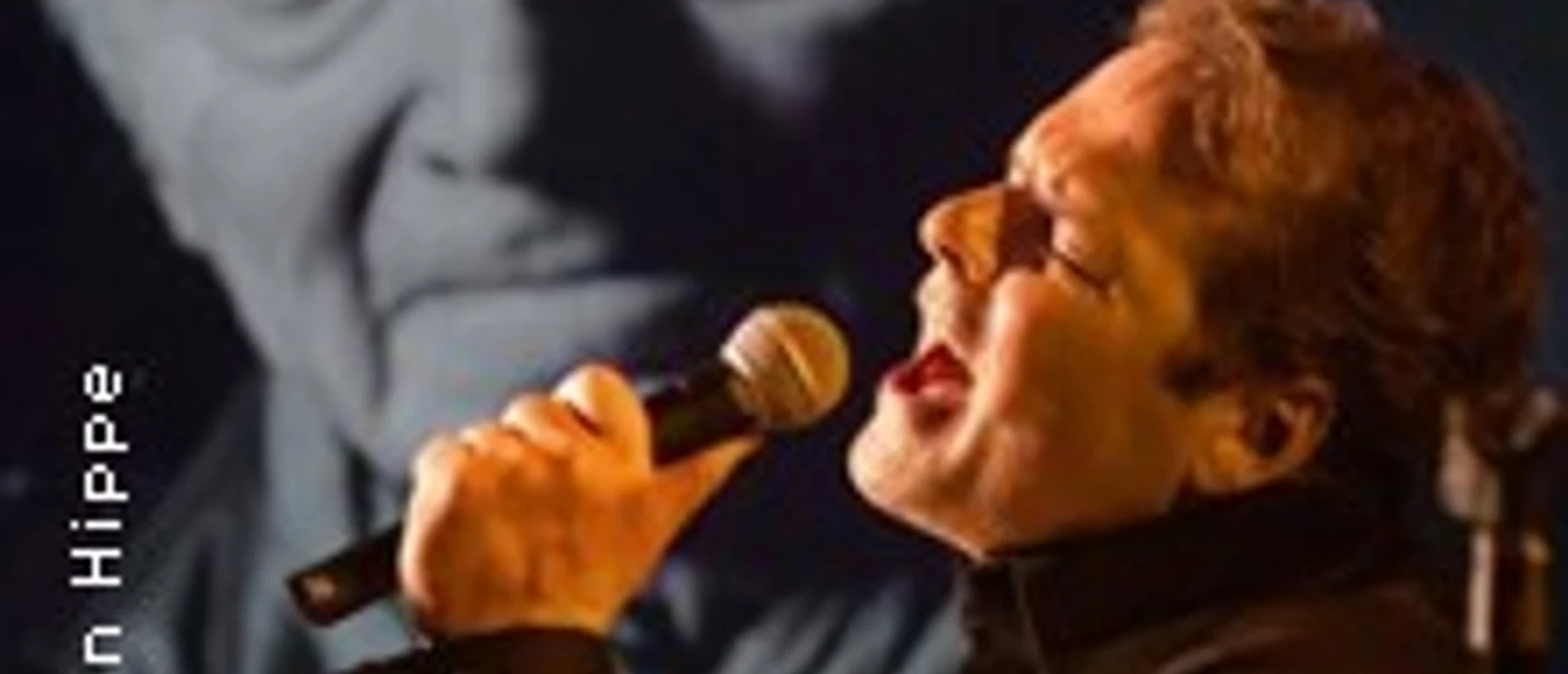Sänger mit Mikrofon vor großem Schwarz-Weiß-Porträt von Charles Aznavour