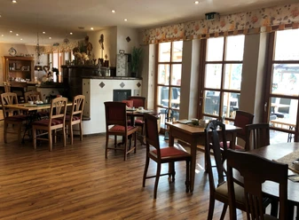 Sitzbereich des Cafés Erlenhof Sitzbereich mit Stühlen und Tischen aus Holz, weißem Kamin im Hintergrund,