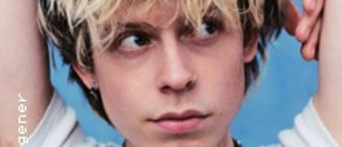 Porträt eines jungen Mannes mit blond zerzaustem Haar vor blauem Hintergrund