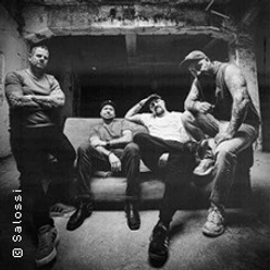 Schwarz-Weiß-Porträt von vier Bandmitgliedern in einem rauen Backstage-Raum