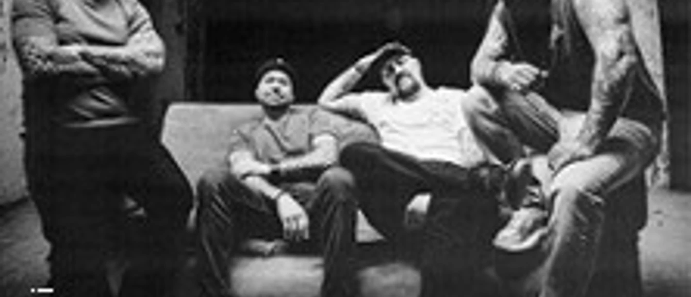 Schwarz-Weiß-Porträt von vier Bandmitgliedern in einem rauen Backstage-Raum