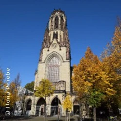 Kirchturm von St. Agnes in Köln mit Herbstbäumen vor blauem Himmel