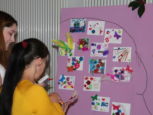 Pinnwand bei der Frauen*Kraft Zwei Frauen basteln bunte Karten an einer rosa Pinnwand beim Frauen*Kraft-Fest.