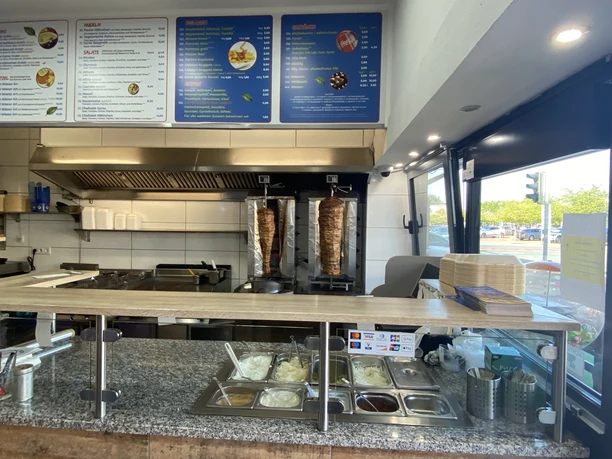 Athena_Grill_Tresen.jpg Tresen des Athena Grill mit Fleischspießen, Saucen und einer Speisekarte im Hintergrund.