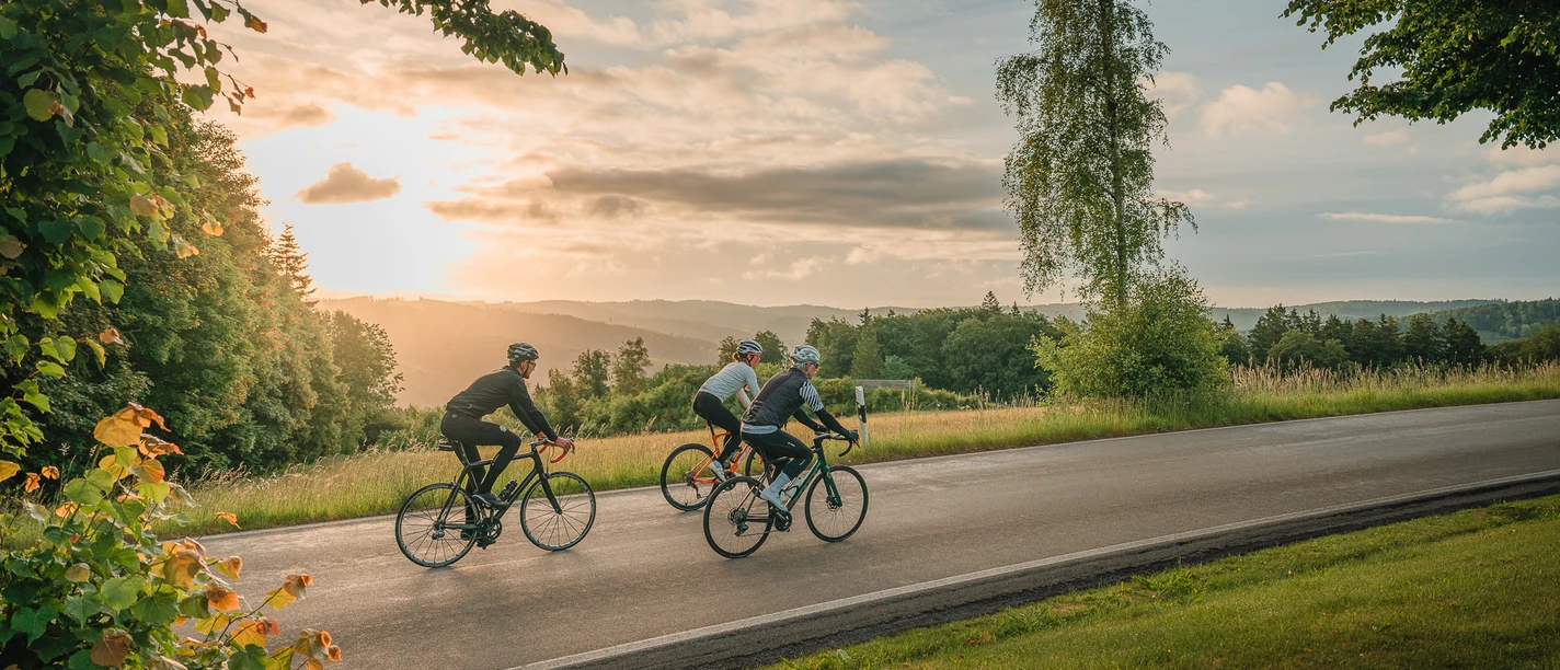 Drei Rennradfahrer auf einer Landstraße im Sauerland bei Sonnenuntergang