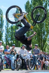 Marc Diekmann.jpg A BMX rider wearing a helmet performs a backward somersault in front of an audience at the pump track.
