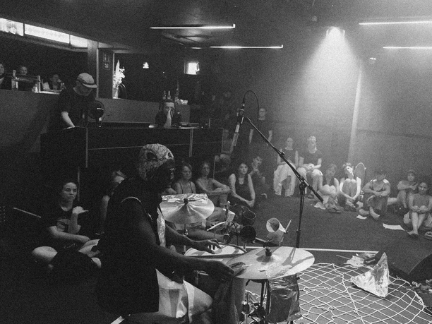 Black-and-white photograph of a concert featuring a drum set and an audience in the Cologne metropolitan area