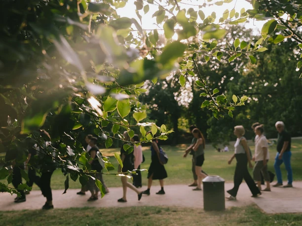 ritual-termin-1-juli-lucie-schulze.jpg Gruppe bei einem Spaziergang im Park, im Vordergrund grüne Blätter im Gegenlicht