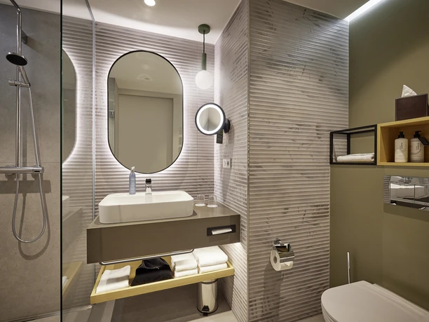 ATLANTIC Hotel Frankfurt_Modern Bathroom Modern bathroom at the ATLANTIC Hotel Frankfurt featuring a walk-in shower, round mirror, sink, and storage surfaces.