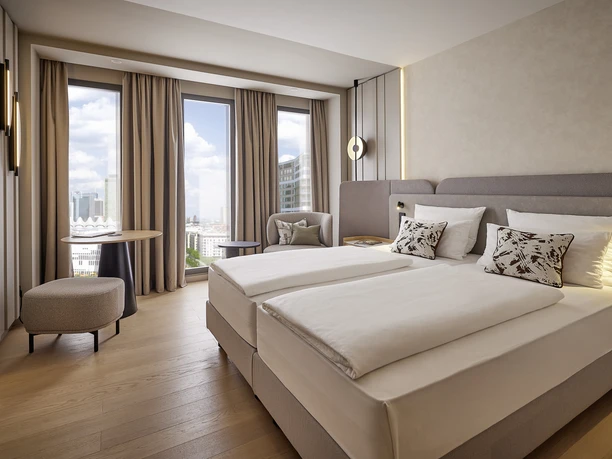 ATLANTIC Hotel Frankfurt_Modern Room A modern room at the ATLANTIC Hotel Frankfurt with two beds, a sitting area, a large TV, and floor-to-ceiling windows overlooking the Frankfurt skyline.