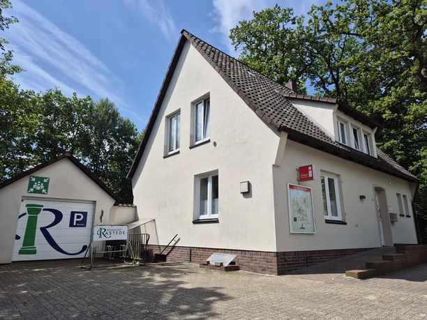 Tourist-Information Rastede in hellem Haus mit Parkplatz und Infotafel.