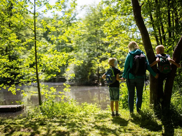 Mutter mit zwei Kindern am Ufer des Diemelsees, umgeben von Bäumen, sie beobachten das ruhige Wasser.