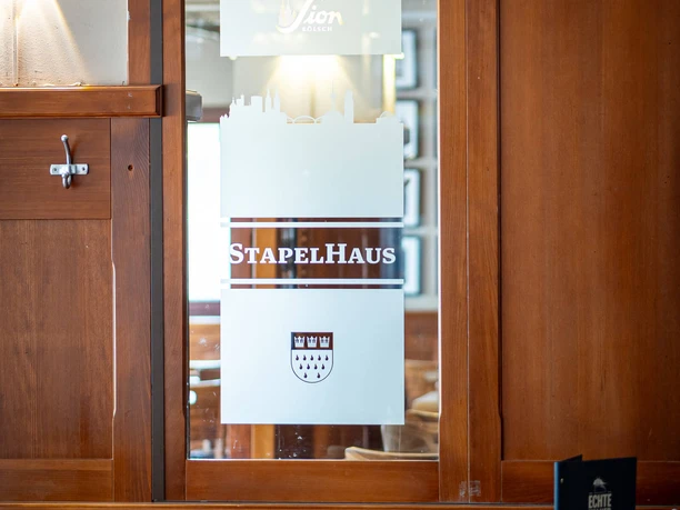Stapelhaus Gastraum im Stapelhaus mit Holzbänken, Tischen und Logo auf matter Glasscheibe