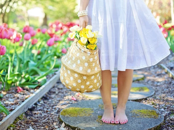 Frühlingsschritte im Blütenparadies Unterkörper einer barfuß laufenden Frau mit weißem Kleid und gelbem Tulpenkorb, entlang eines Tulpenbeets