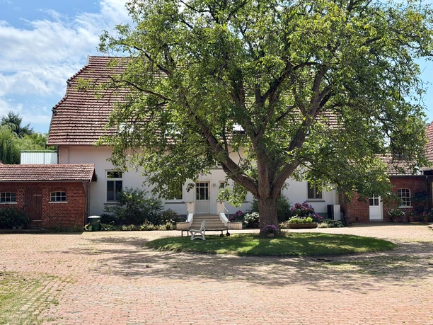 A view of the Riederhof farmyard with a large tree, brick buildings, and a white house.