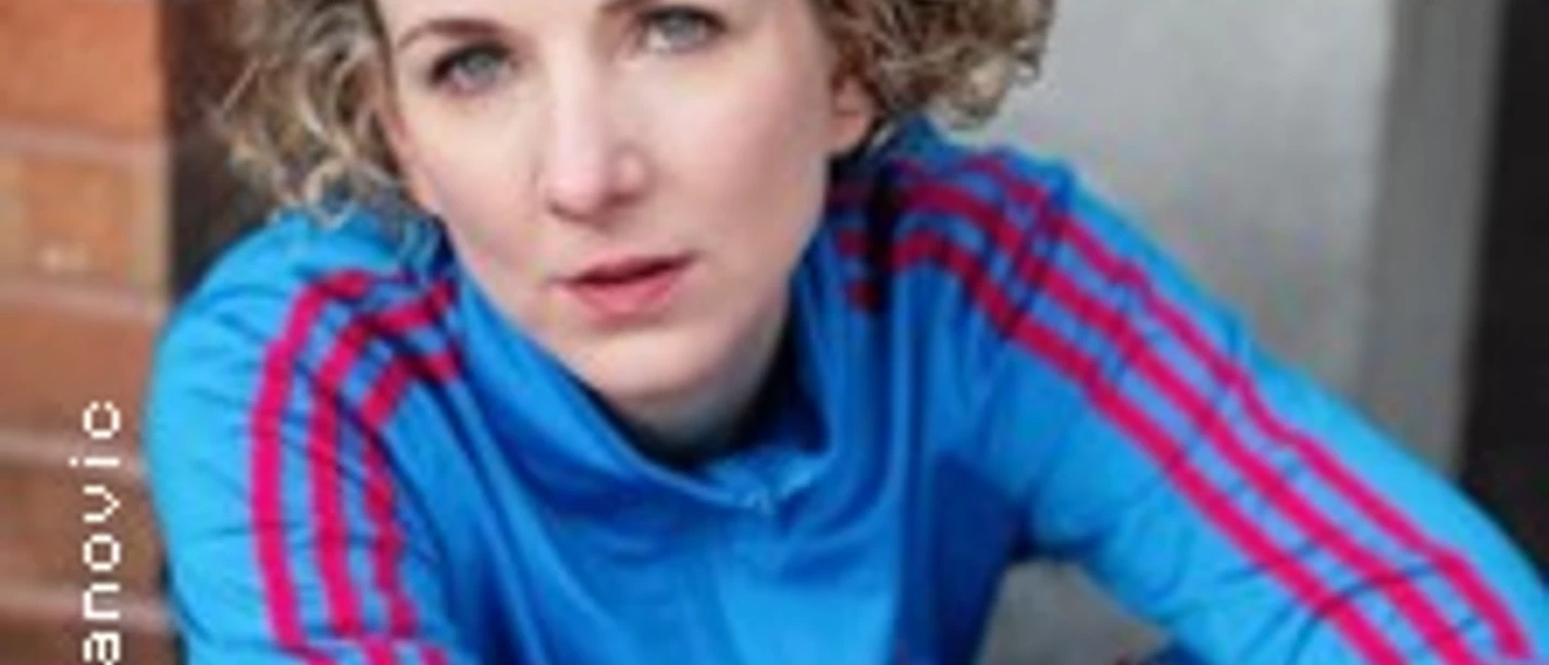 Porträt einer Frau mit lockigem Haar im blauen Pullover, an eine Wand gelehnt