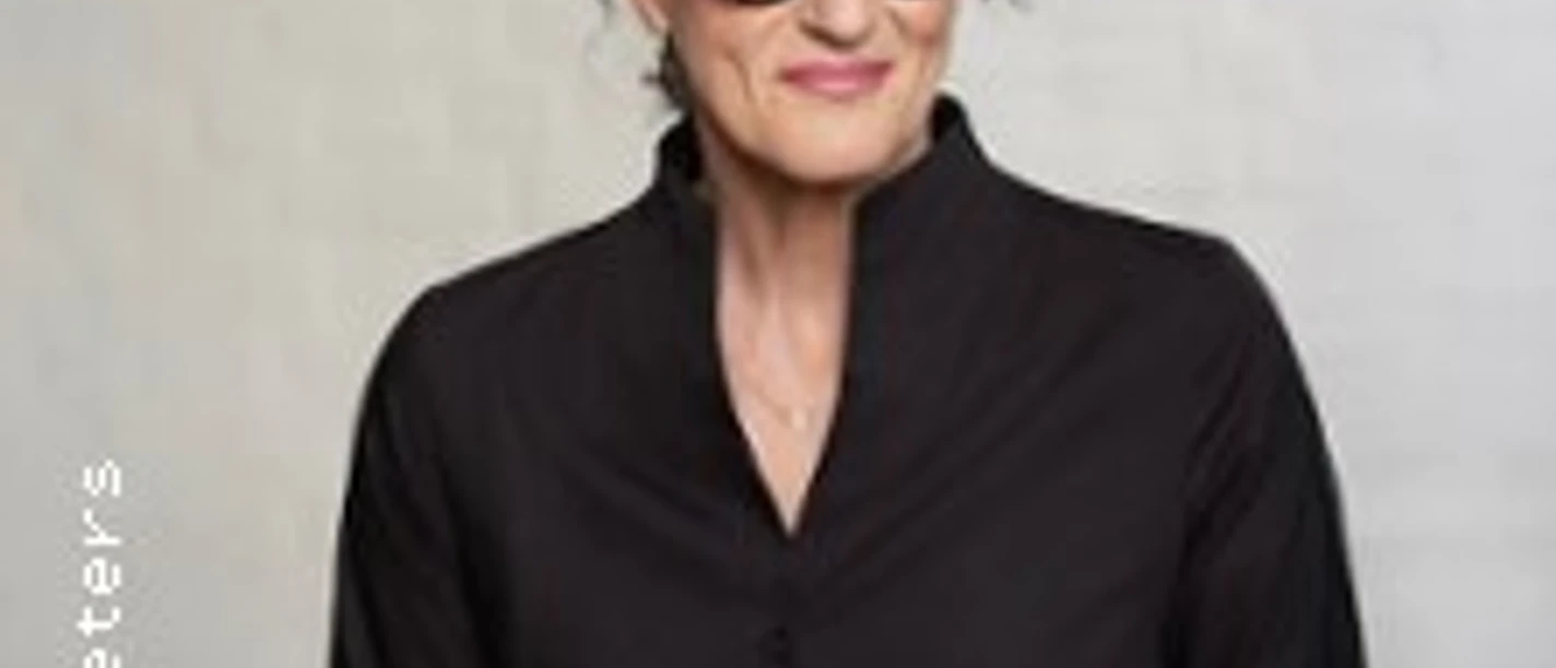 Porträt von Birgit Süss mit runder Brille und schwarzer Bluse vor hellem Hintergrund