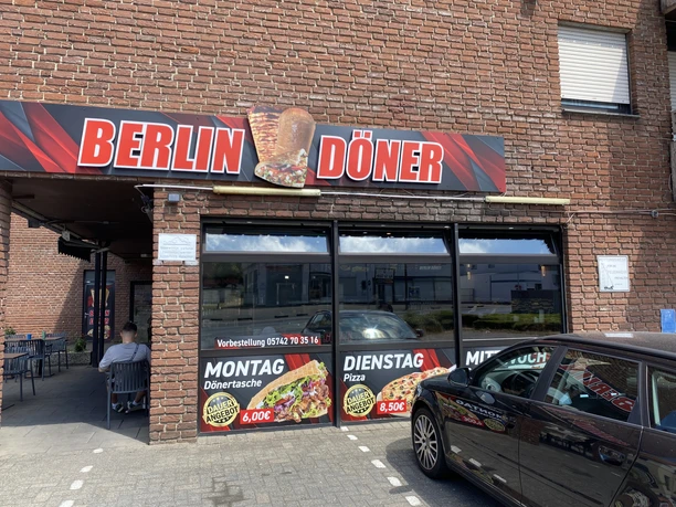 Berlin Döner_Pr. Oldendorf_Außenansicht_quer.jpg Außenansicht des Imbisses Berlin Döner mit rotem Werbeschild und Angeboten an der Glasfassade.