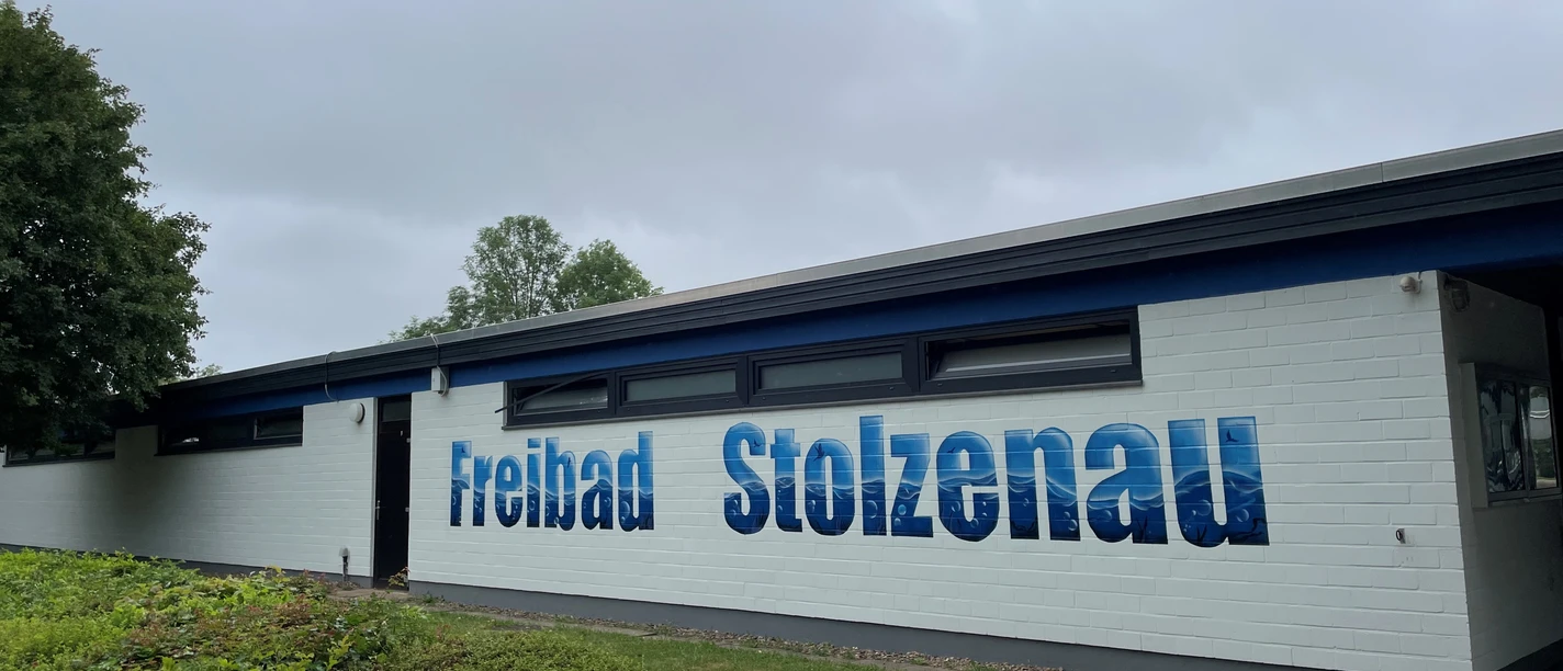 Freibad Stolzenau.jpg Außenansicht des Freibads Stolzenau mit blauem Schriftzug an weißer Fassade.