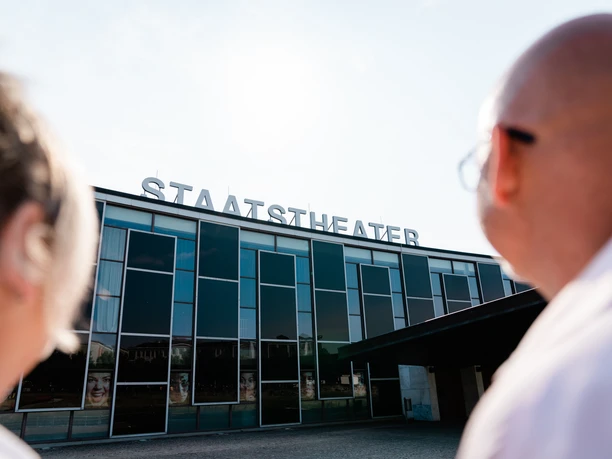 Staatstheater Kassel Ein Pärchen schaut zum Staatstheater Kassel. Auf dem Gebäude steht in weißer Schrift auf dem Dach "Staatstheater".