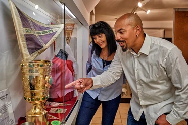 RheinMain Offenbach - OFCKickersFanMuseum Besuchende im OFC Kickers Fan Museum vor einer Vitrine