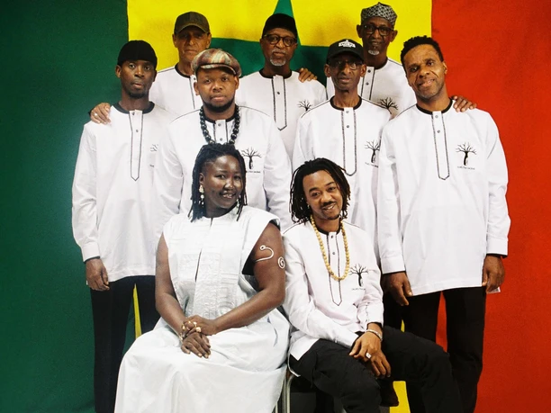 Orchestra Baobab Orchestra Baobab in weißen Outfits vor grün-gelb-rotem Hintergrund beim Festival MitAfrika