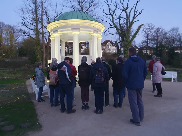 Gruppe bei einer Literaturwanderung vor beleuchtetem Pavillon im Kurpark bei Dämmerung