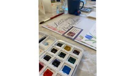 Handlettering-trifft-watercolor_bispingen.jpg Aquarellfarben, Pinsel und Handlettering-Vorlage auf einem Workshop-Tisch.