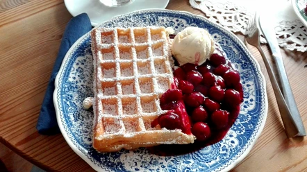 Bergische Waffel mit Puderzucker, heißen Kirschen und Vanilleeis auf blauweißem Teller