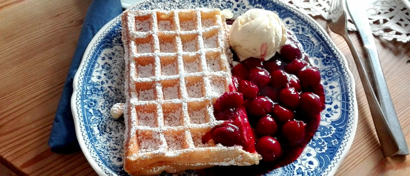 Bergische Waffel mit Puderzucker, heißen Kirschen und Vanilleeis auf blauweißem Teller