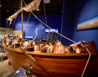 BIMU - Boot Kinder sitzen in einem Holzboot in einer Museumsausstellung