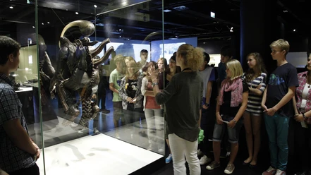 DFF - Dauerausstellung Gruppe bei Führung vor Alien-Figur in Museumsvitrine