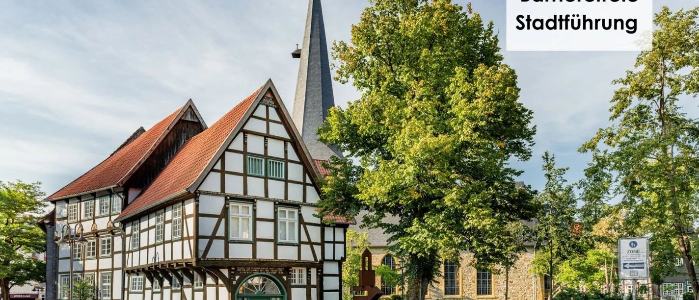 Historisches Fachwerkhaus Verhoffhaus in Gütersloh mit Kirchturm und Baum im Hintergrund.