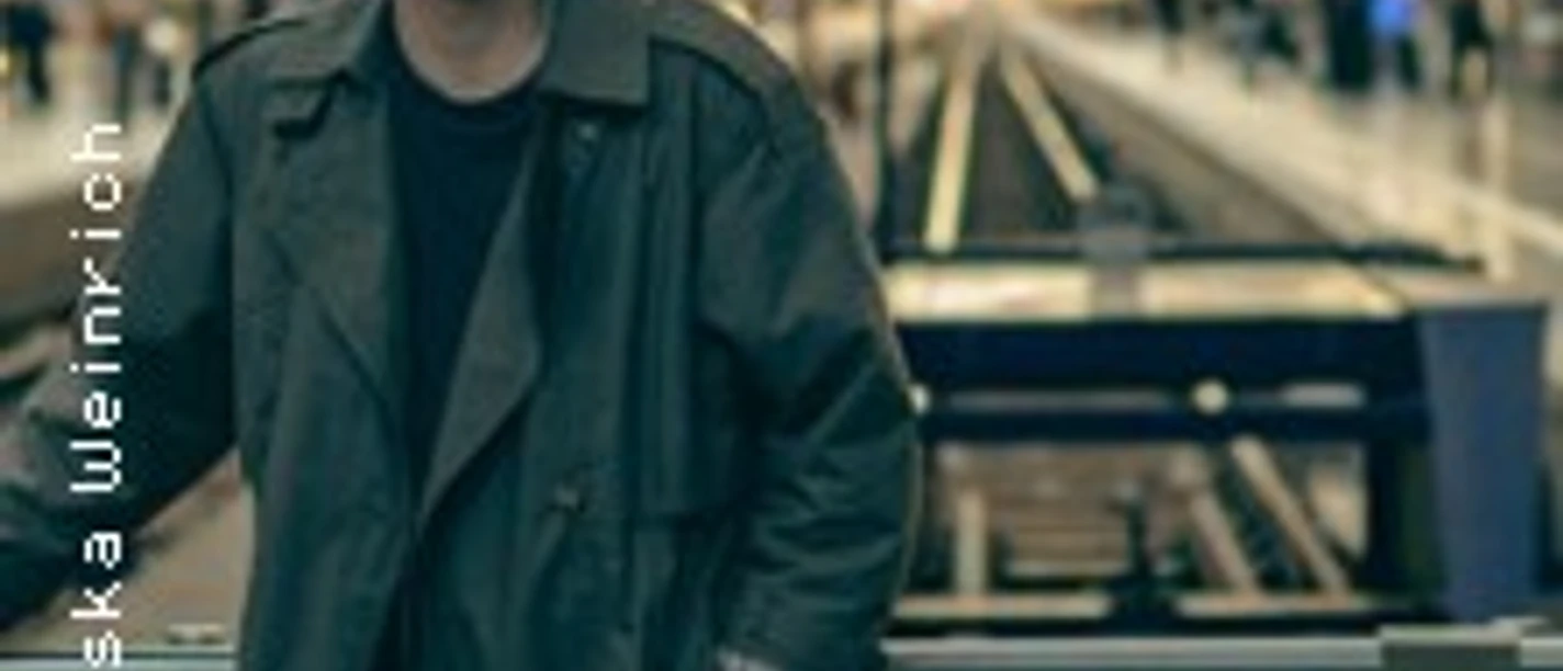 Nils Brunschede steht in dunklem Mantel an einem Bahnsteig mit Gleisen im Hintergrund