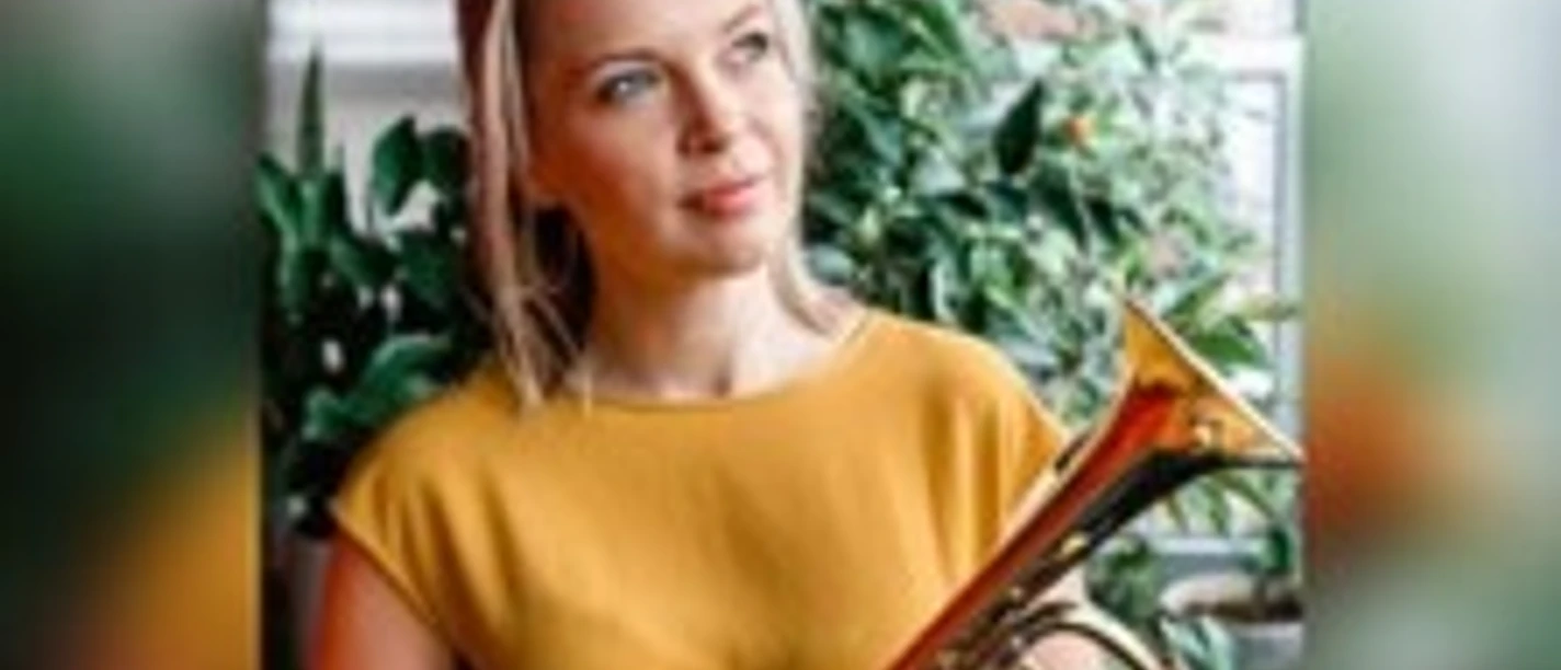 Porträt von Bria Skonberg im gelben Oberteil mit Trompete vor grünen Pflanzen