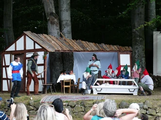 Schneewittchen im gläsernen Sarg – Szene aus dem Märchen auf der Naturbühne Bergfreiheit Sieben Zwerge und der Prinz stehen auf einer Freilichtbühne um den gläsernen Sarg von Schneewittchen