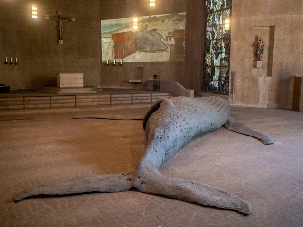 Exhibition: GESTRANDET / The Cast Whale Project Whale sculpture in St. Gertrud, in front of the altar, a stained-glass window, and a projected coastal scene