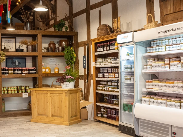 Innenraum des Hofladens mit Holzregalen, Verkaufstheke und Kühlvitrine vor Fachwerkwand.