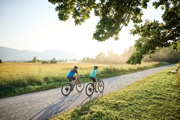Radfahren_Murnauer Moos Zwei Radfahrende auf Kiesweg im Murnauer Moos, mit Wiesen, Bäumen und Bergblick