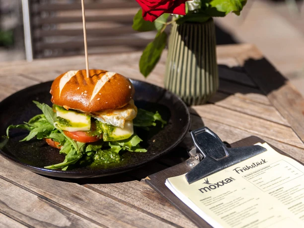 Frühstück im moxxa.caffè Frühstücksburger auf schwarzem Teller mit Speisekarte und roter Rose auf Holztisch