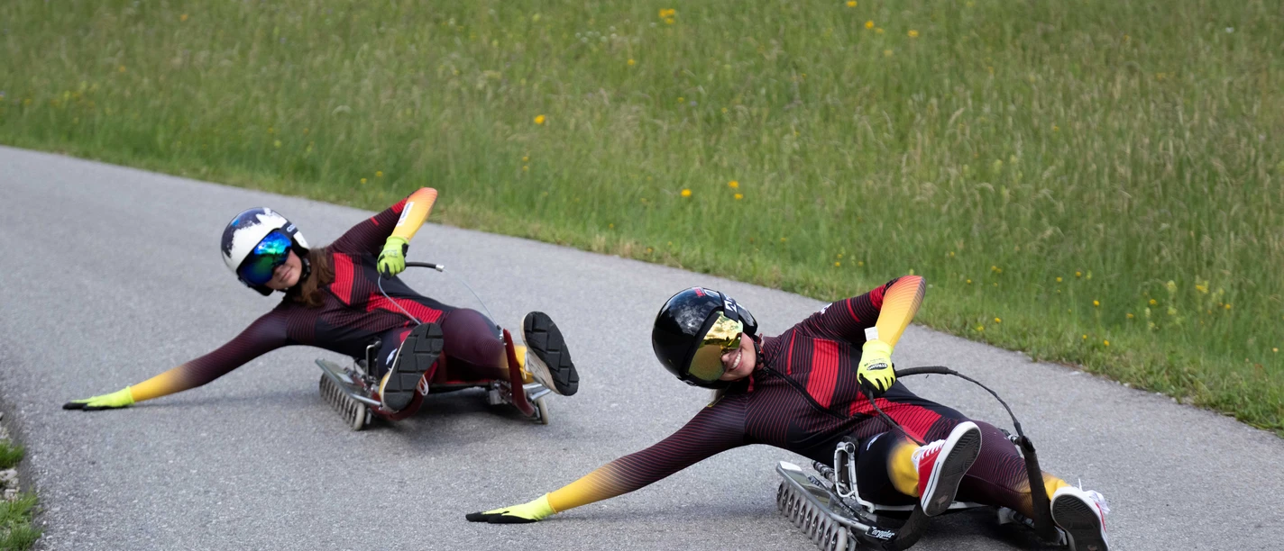 Zwei Rollenrodler in Rennanzügen liegen tief in einer Kurve auf der Asphaltbahn