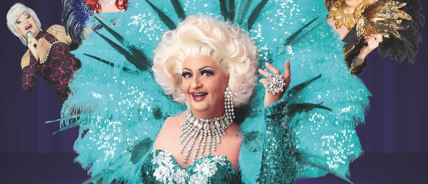 Travestiekünstler in funkelnden Kostümen mit Federn vor violetter Bühnenkulisse