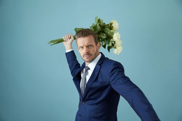 Endlich Glücklich Florian Schroeder im blauen Anzug hält weiße Rosen über der Schulter