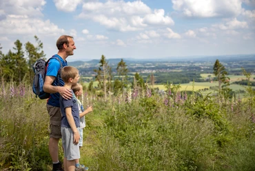 Wandern im Wiehengebirge Vater und zwei Söhne blicken von einer blühenden Wiese über das Wiehengebirge.