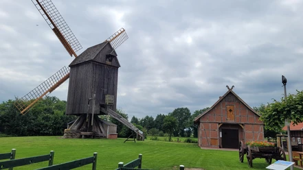 Bockwindmühle Wehe Bockwindmühle und Fachwerkhaus auf einer grünen Wiese unter bewölktem Himmel.