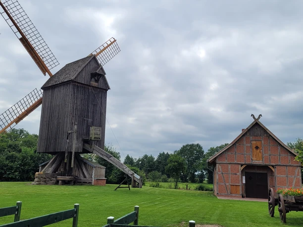 Bockwindmühle Wehe Bockwindmühle und Fachwerkhaus auf einer grünen Wiese unter bewölktem Himmel.