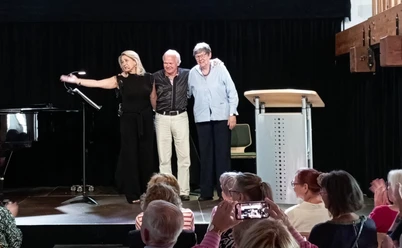 Johanna Holtsteger Drei Mitwirkende auf der Bühne, Publikum applaudiert, daneben Flügel und Redepult.